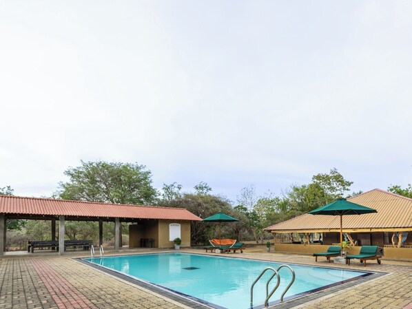 A swimming pool with lounge chairs and umbrellas, surrounded by trees and covered structures. - Joe's Bungalow Yala (Kirinda)