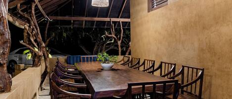 A dining area with a long wooden table, multiple chairs, and a hanging light fixture.