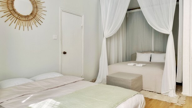 A bedroom with a bed, a bedside table, a nightstand, a canopy bed, a wall-mounted mirror, and a door. - 1BR Demure Design Urban Living Space (Helsinki)