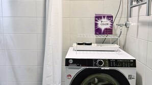 A compact laundry area with a front-loading washing machine, a drying rack, and a shower curtain. - 1BR Demure Design Urban Living Space (Helsinki)