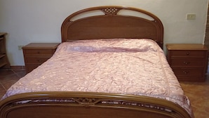 A bedroom with a wooden bed, two nightstands, and a wall-mounted light.