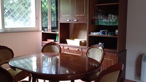 A dining area with a round wooden table and six chairs, surrounded by wooden cabinets and shelves with kitchenware.