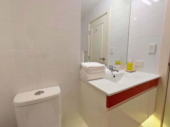 Casa de banho moderna com sanita branca, lavatório com espelho e armário vermelho.