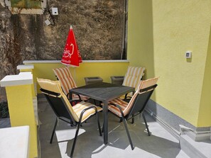 Um pátio externo com mesa, cadeiras, um guarda-sol vermelho e uma parede texturizada.