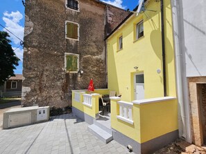 Un immeuble à la façade jaune, doté d’un balcon avec des balustrades blanches et d’un drapeau rouge.