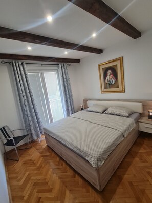 Un dormitorio con una cama grande, una mesita de noche, una silla y una ventana con cortinas.