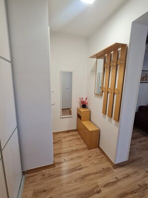 Een kamer met een houten vloer, een spiegel, een klein houten kastje en een deur.