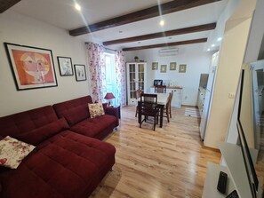 Een woonkamer met een rode bank, een eettafel met stoelen en een keuken met apparatuur.