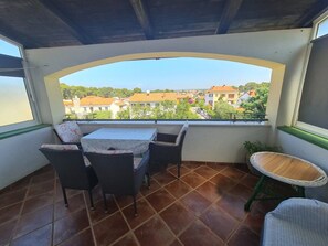 Un patio cubierto con mesa y sillas, una pequeña mesa redonda y vistas a una zona residencial.