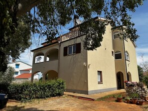 A two-story building with a beige facade, arched windows, and a stone wall with potted plants. - Apartment Branko I with balcony and sea view in Porec, Istria (Mugeba)