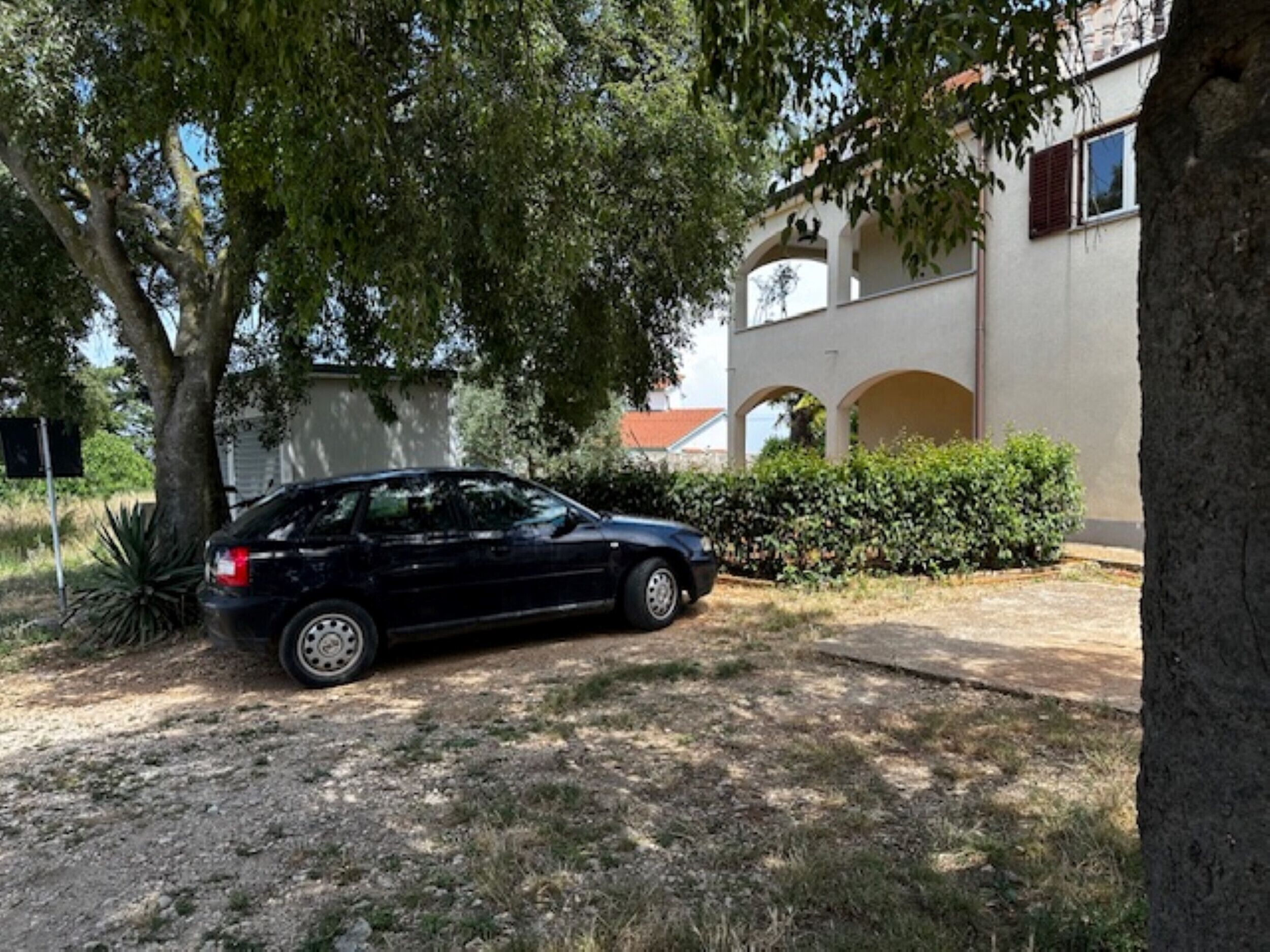Une voiture noire est garée dans une allée, avec un arbre et un bâtiment en arrière-plan.