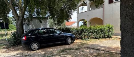 Une voiture noire est garée dans une allée, avec un arbre et un bâtiment en arrière-plan.