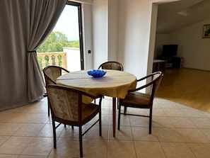 Un coin repas avec une table ronde, quatre chaises, un bol bleu et une fenêtre avec des rideaux.