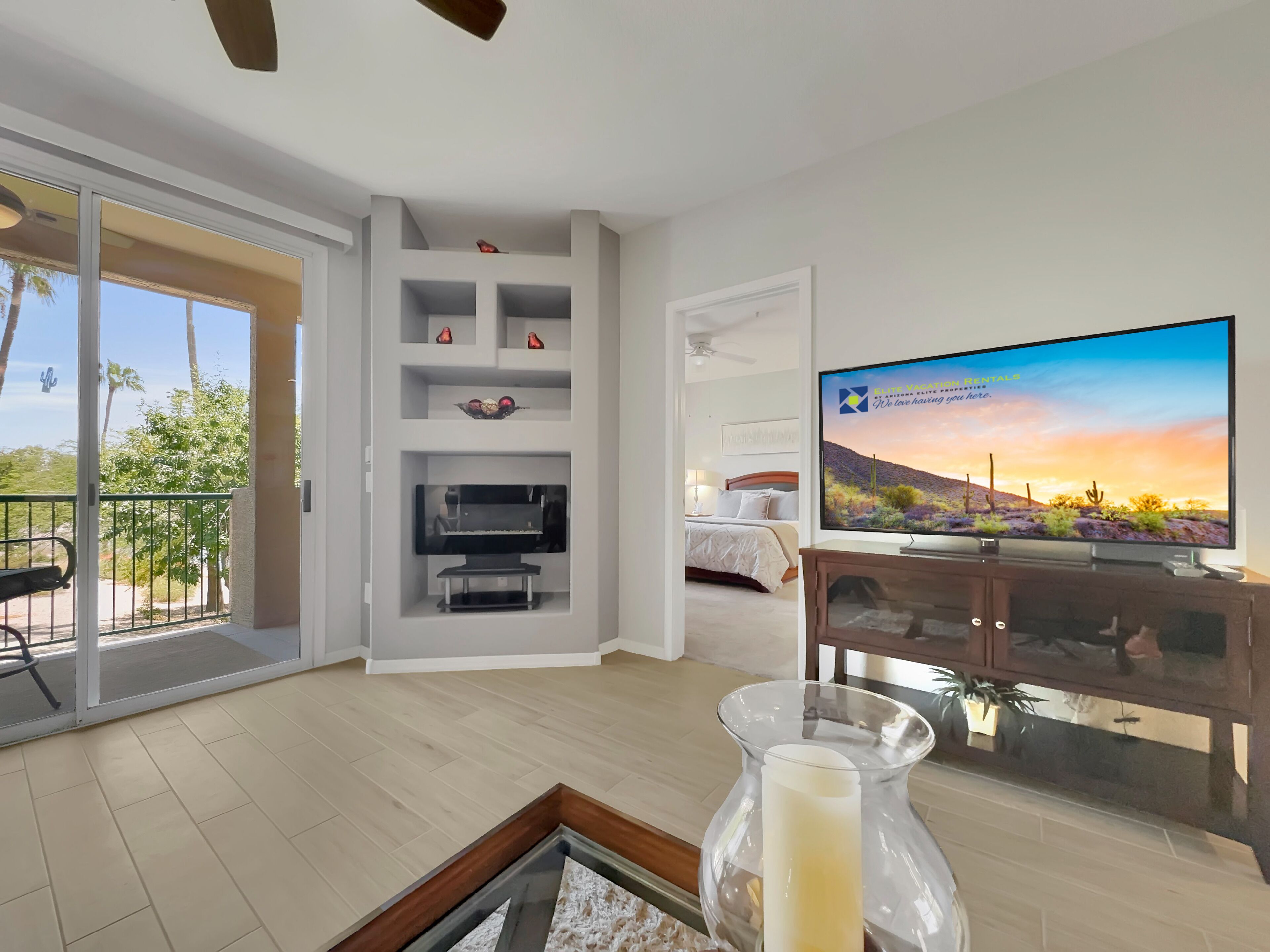 A modern hotel room with a balcony, a flat-screen TV, a bed, and a TV stand with decorative items.