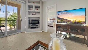 A modern hotel room with a balcony, a flat-screen TV, a bed, and a TV stand with decorative items. - 2BR condo w golf course views, balcony (Mesa)