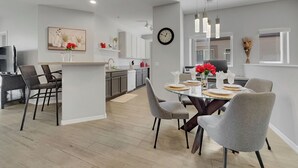 A modern kitchen with white cabinets, a dining area with a round glass table, and grey chairs. - 2BR condo w golf course views, balcony (Mesa)