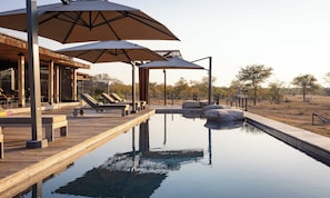 Un espace piscine agrémenté de chaises longues et de parasols, entouré d’une terrasse en bois et offrant une vue sur le paysage.