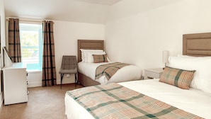 A hotel room with a bed, a desk, a chair, and a window with curtains. - Loch Ness Gate House Apartments (Fort Augustus)