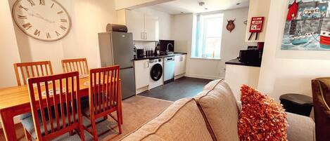 A compact living space with a dining area, kitchenette, and a sofa with decorative pillows.