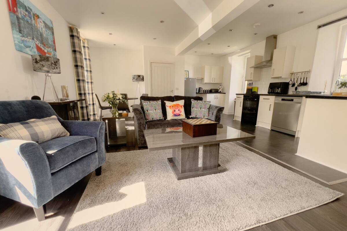 A spacious living room with a blue sofa, a coffee table, and a kitchen in the background.