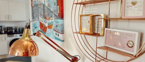 A modern interior with a copper desk lamp, a colorful maritime painting, and framed inspirational quotes on a wall.