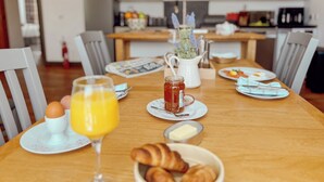 A breakfast setting with a wooden table, plates, a glass of orange juice, a jar of honey, croissants, and a newspaper. - Loch Ness Gate House Apartments (Fort Augustus)