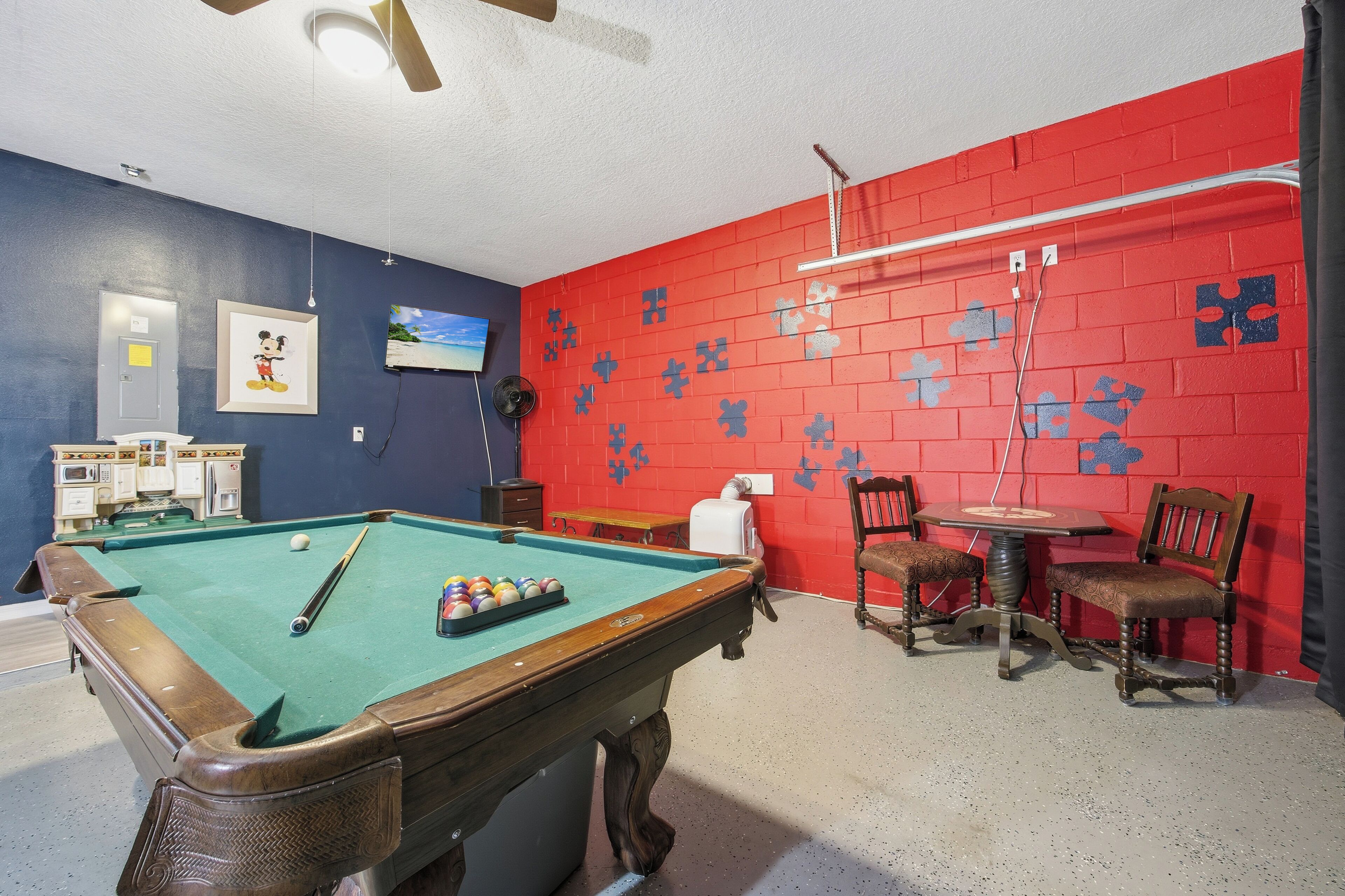A pool table with balls, a television, and a red brick wall with puzzle pieces.