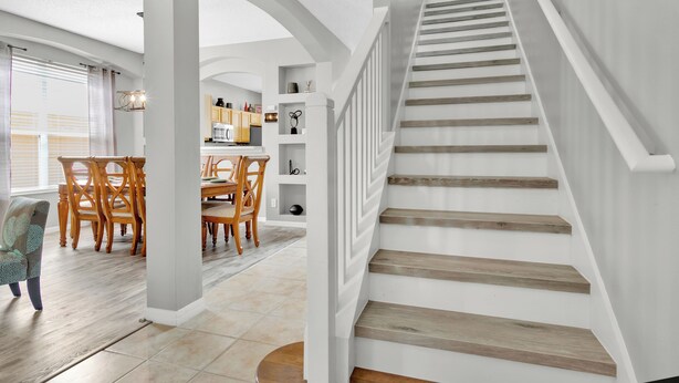 A spacious living area with a staircase, wooden flooring, and a dining area with chairs and a table. - Free Pool Heat!  Stunning Pool Home - No Rear Neighbors - 5 Minutes To Disney! (Kissimmee)