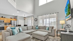 A spacious living area with a sectional sofa, a dining table, and a kitchen in the background. - Free Pool Heat!  Stunning Pool Home - No Rear Neighbors - 5 Minutes To Disney! (Kissimmee)