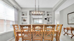 A dining area with a wooden table and chairs, a chandelier, and shelves with decorative items. - Free Pool Heat!  Stunning Pool Home - No Rear Neighbors - 5 Minutes To Disney! (Kissimmee)