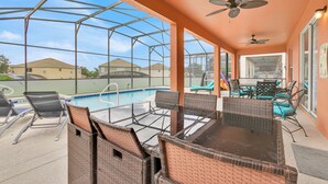 A covered outdoor area with a pool, wicker furniture, ceiling fans, and a view of neighboring houses. - Free Pool Heat!  Stunning Pool Home - No Rear Neighbors - 5 Minutes To Disney! (Kissimmee)