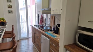 Una cocina compacta con armarios de madera, lavavajillas integrado, microondas y un pequeño comedor con una silla.