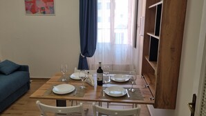 Un comedor con una mesa de madera preparada para cuatro personas, una botella de vino y una cortina azul.