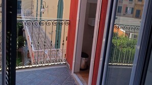 Un balcón con suelo de baldosas, barandilla de metal y vistas a edificios cercanos.