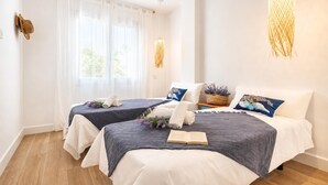 Habitación de hotel con dos camas, un ventanal con cortinas traslúcidas, un ventilador de techo y una lámpara colgante.