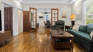 Un salon spacieux doté d’un parquet, d’un canapé à motifs verts, d’une table basse en bois et d’un ventilateur de plafond.