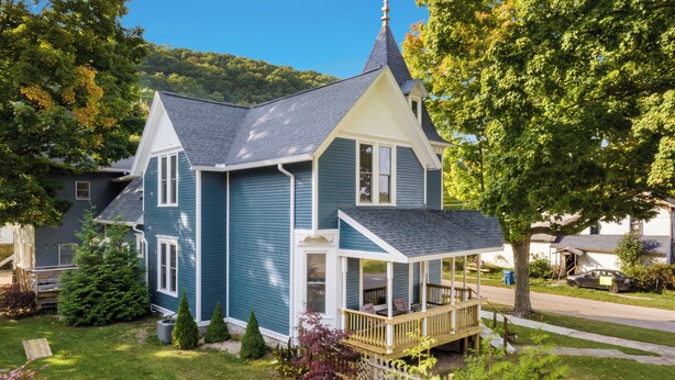 Une maison à deux étages avec un porche, entourée d’une pelouse bien entretenue et d’arbres.