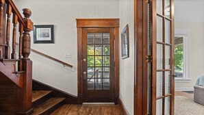 Un escalier en bois menant à une porte dotée d’un panneau de verre, un tableau encadré accroché au mur et un tapis sur le sol.
