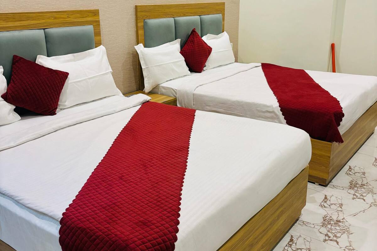 Two beds with wooden frames and grey headboards, white bedding, and red throw pillows.