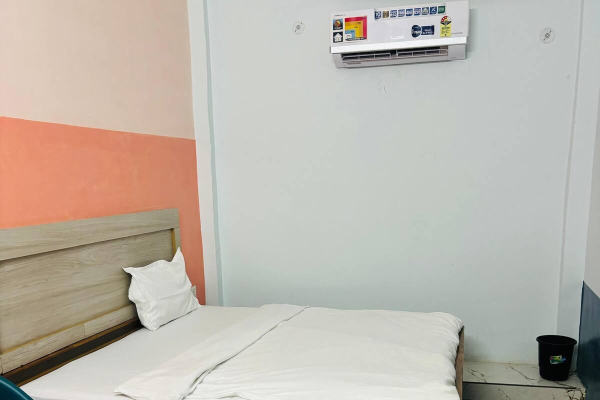 A single bed with a wooden headboard, a white mattress, and a white pillow. There is a black trash bin to the right of the bed.