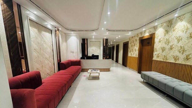 A spacious lobby with a red sofa, a grey sofa, and a reception desk. - Maharishi Inn (Faizabad)