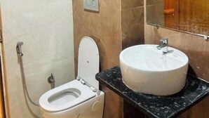 A bathroom with a white toilet, a sink with a black countertop, and a mirror above the sink. - Maharishi Inn (Faizabad)