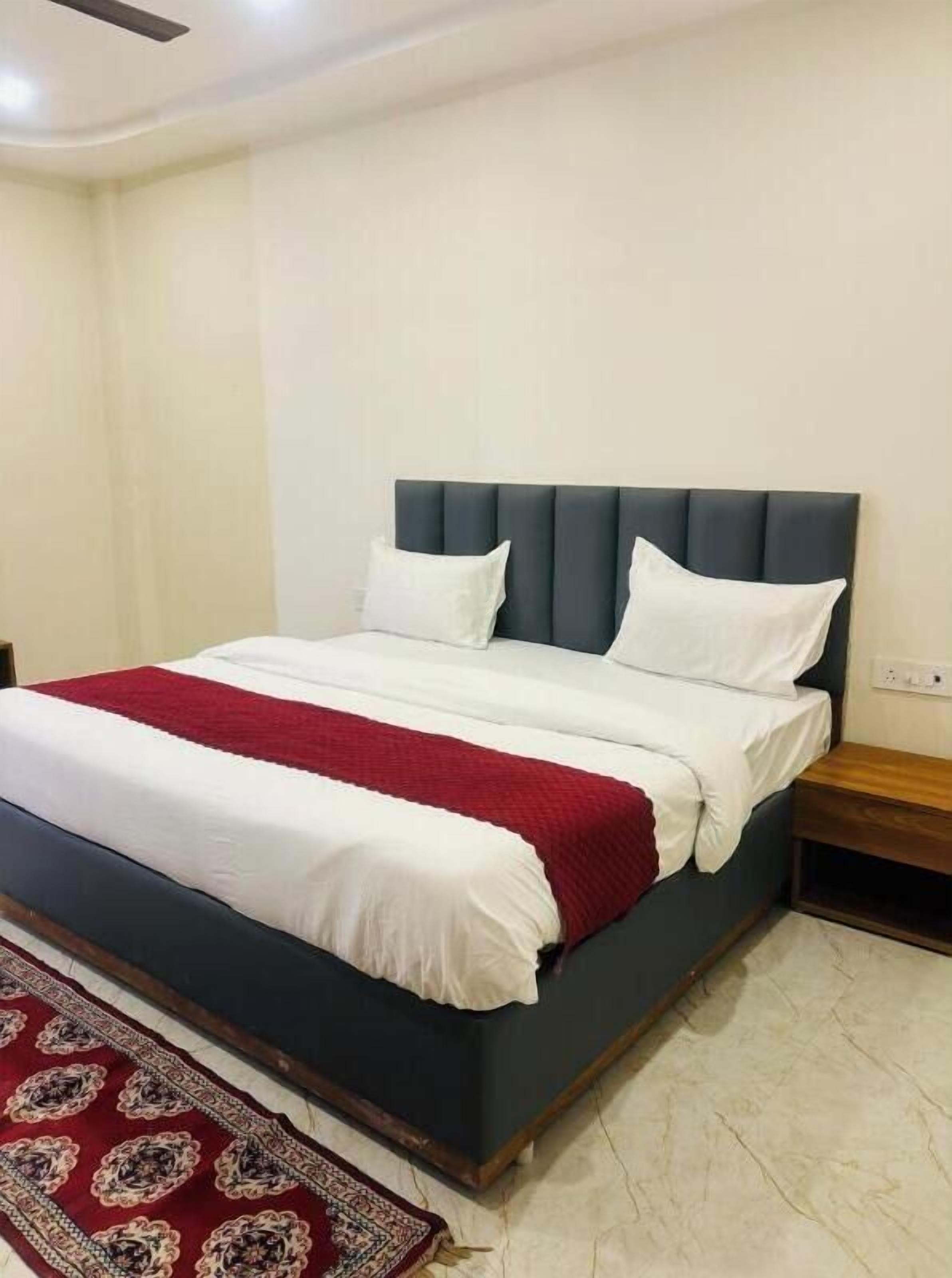 A neatly made bed with white and red bedding, a dark headboard, and a wooden nightstand beside it.