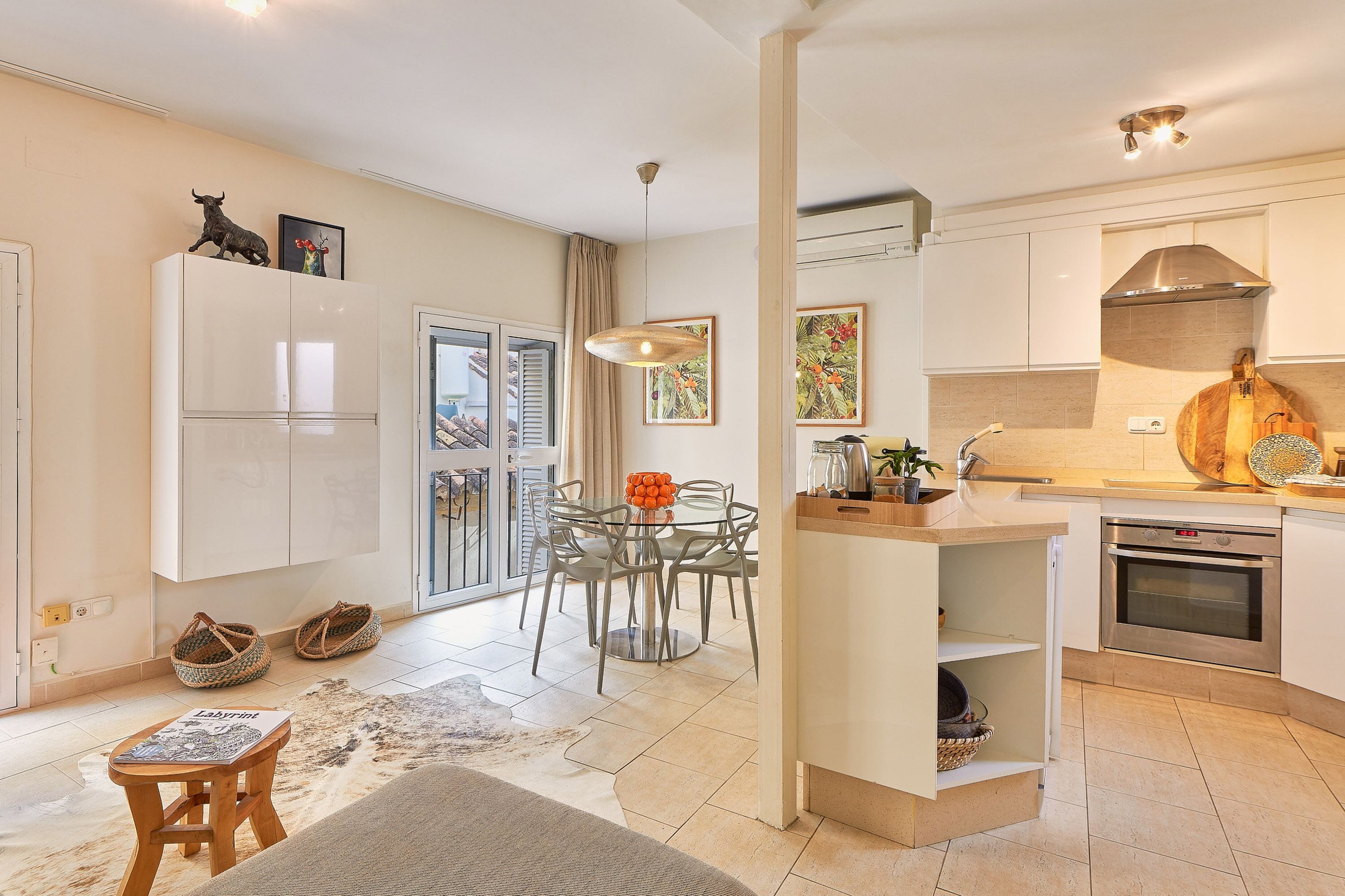 A modern kitchen with white cabinets, a built-in oven, and a dining area with a glass table and chairs.