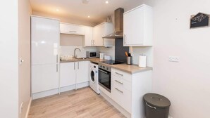A compact kitchen with white cabinets, a microwave, a stove, and a washing machine. - IBEX HOUSE | Fully Equipped 2-Bed | Free Parking (Berkshire)