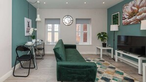 A modern living room with a green sofa, a dining table with chairs, a TV, and a clock on the wall. - IBEX HOUSE | Fully Equipped 2-Bed | Free Parking (Berkshire)