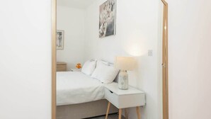 Une chambre à coucher avec un lit, une table de chevet, une lampe et une œuvre d’art accrochée au mur.