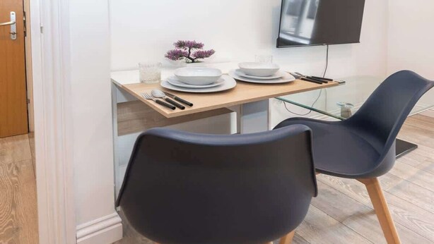 Un coin repas avec une table en bois, deux chaises noires et une petite plante décorative.