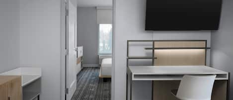 A modern hotel room with a bed, a desk, a chair, and a TV mounted on the wall.