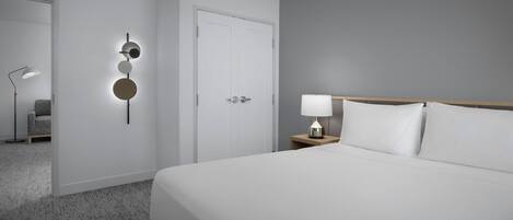 Camera d'albergo con un letto grande, un comodino con una lampada, un punto luce a parete e una porta.